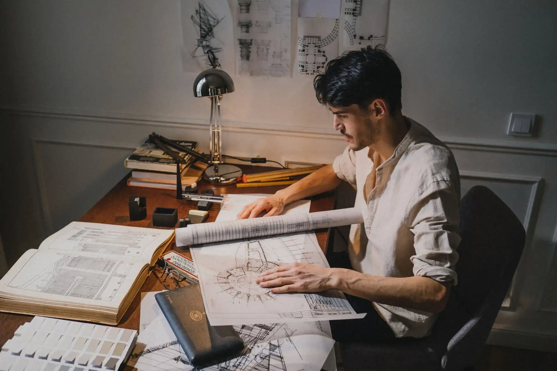 A single practitioner at a drafting table, working through plans under a lamp